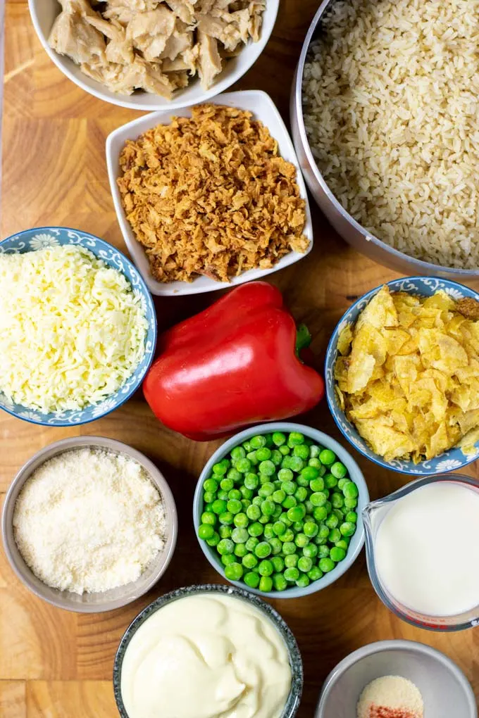 Ingredients needed for making the Chicken and Rice Casserole are assembled in small bowls on a wooden board. 