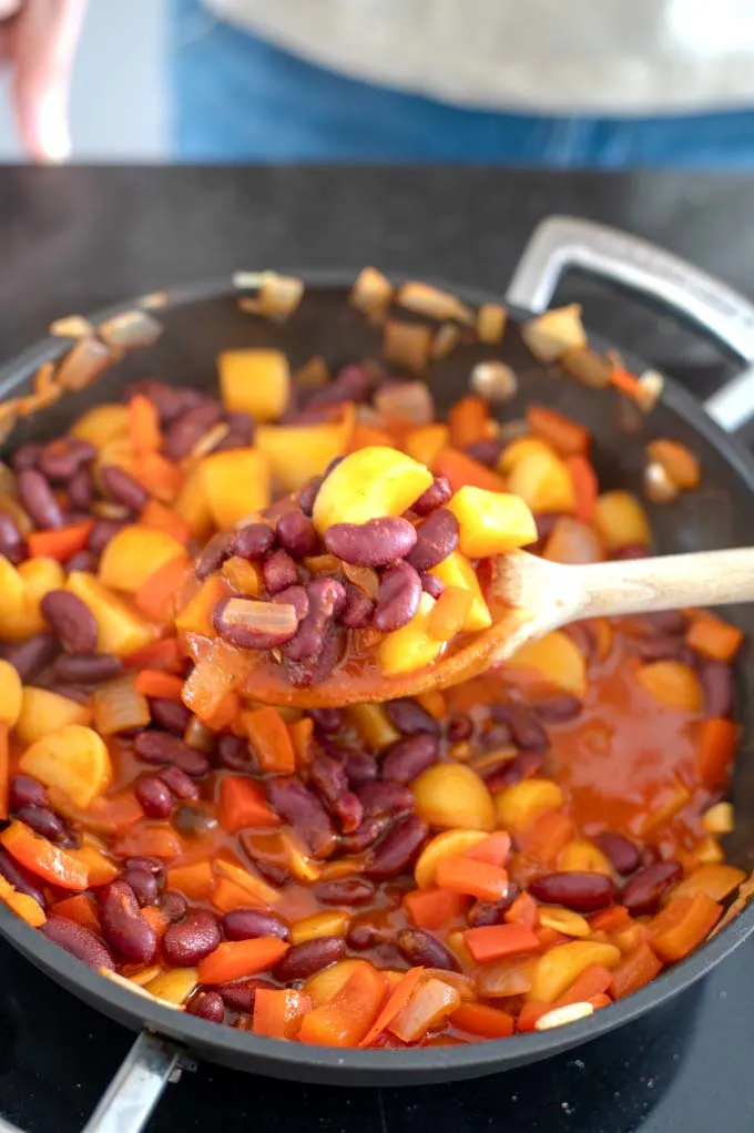Spoonful of beans are taken from the pan while cooking.