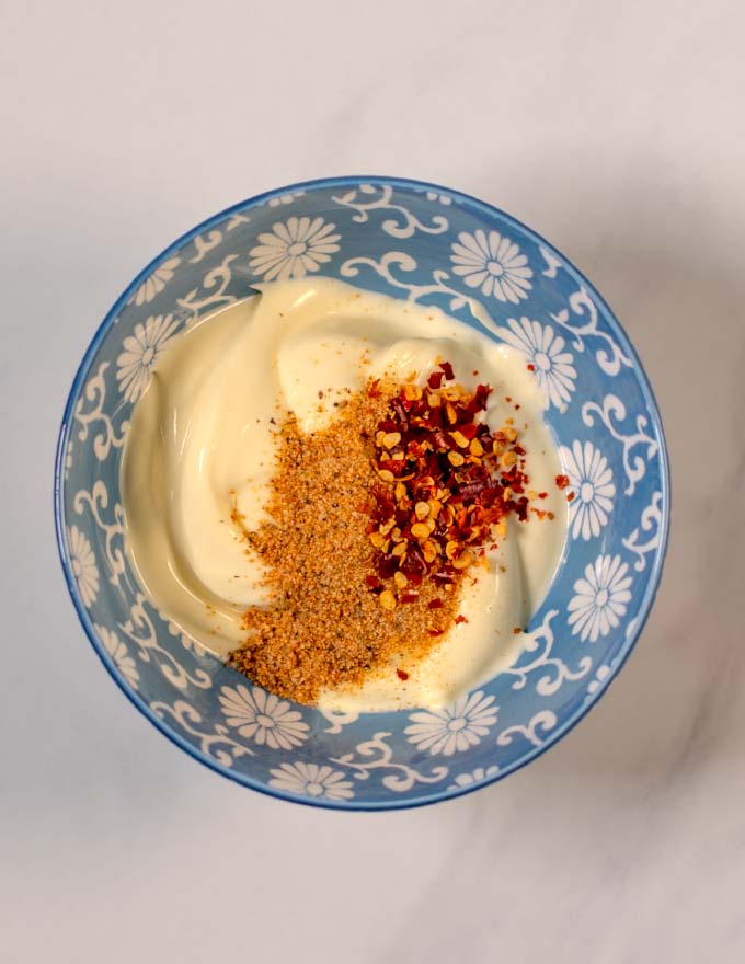 Top view of a mixing bowl with plain mayo, Cajun seasoning, and chili flakes.