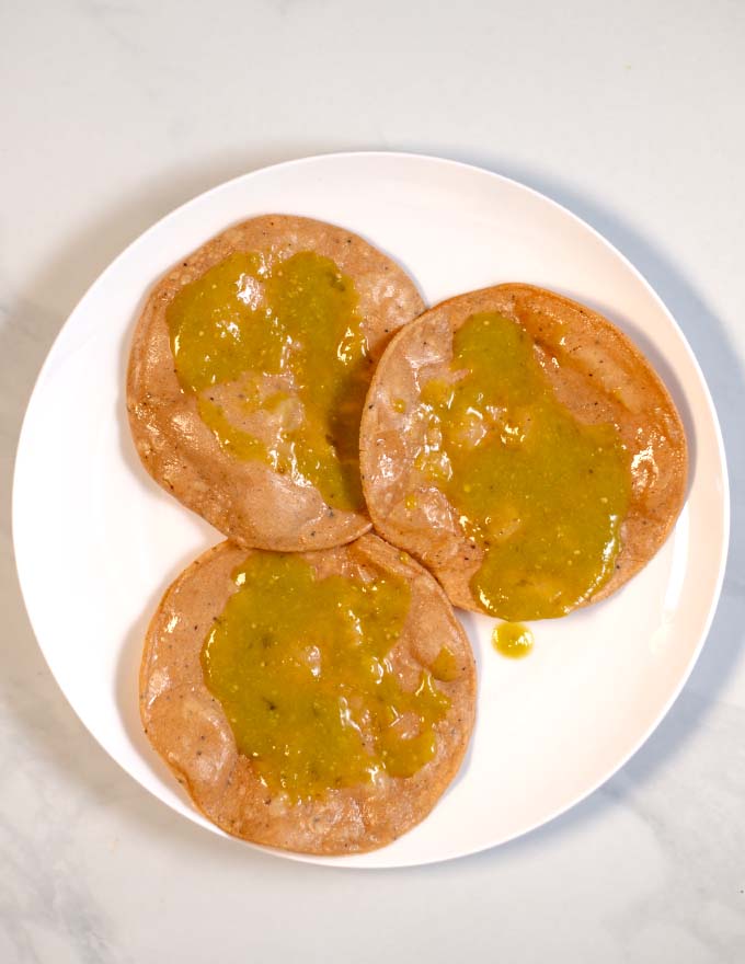 Tomatillo salsa verde is spread on fried tortillas. 