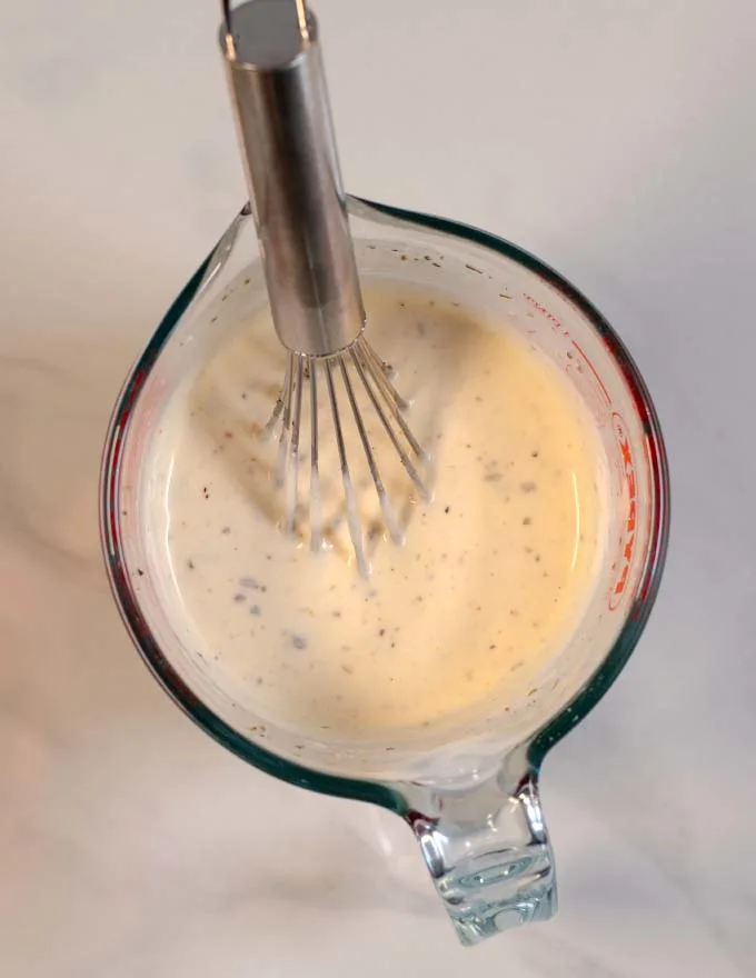 Top view on a mixing bowl with creamy sauce and a wire whisk.