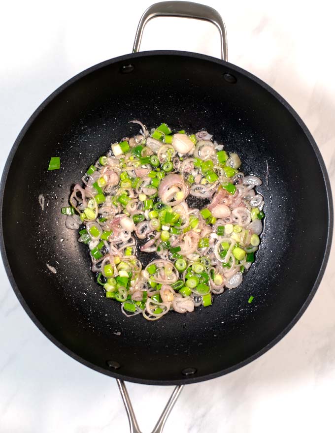 View of a wok in which onions and scallions are fried.