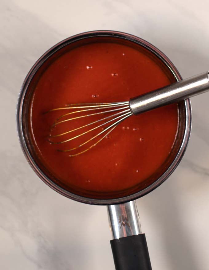 Whisking the Currywurst sauce in a small saucepan while simmering.