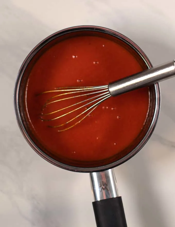 Whisking the Currywurst sauce in a small saucepan while simmering.