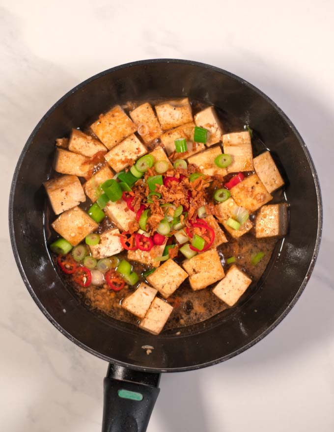 Sauce, spices, scallions, and red pepper are given into the pan with tofu.