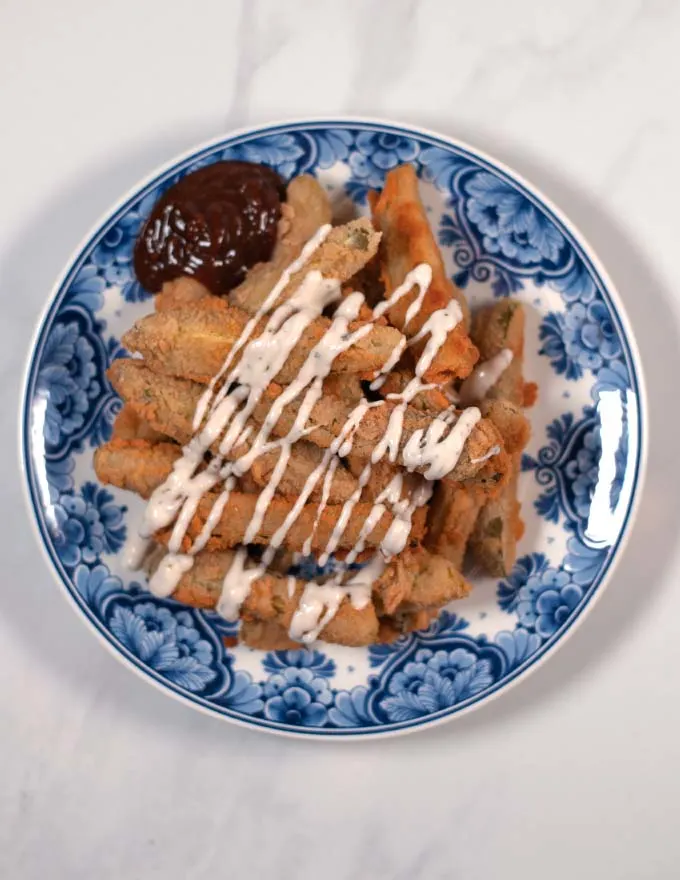 Top view on a blue plate with pickle fries served with sauces.