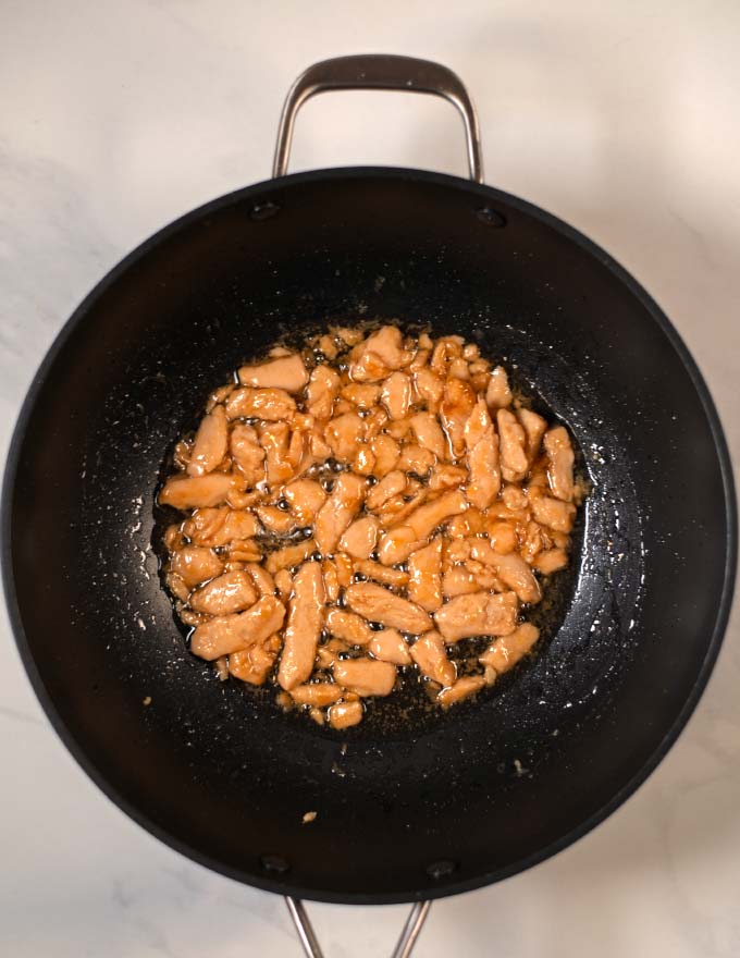 Marinated chicken is fried in a wok.