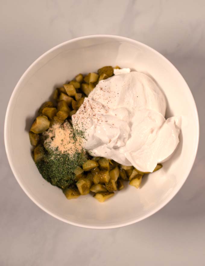 Chopped pickles, sour cream, herbs and spices are given ti a mixing bowl.