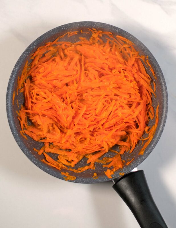 Shredded carrots are fried in a small pan