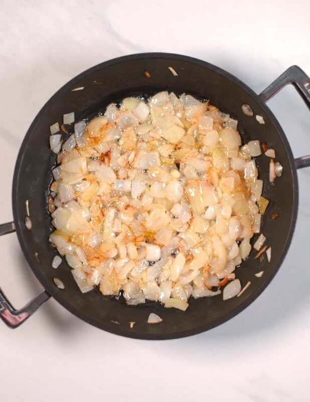 Onions are sautéed in a pan.