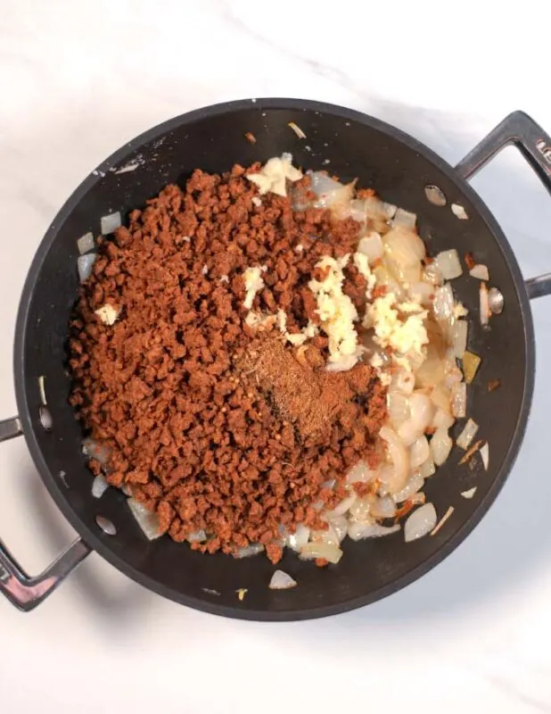 Ground beef and spices are added to the onions in a pan.