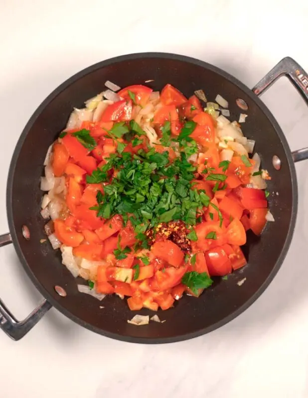 Tomatoes, spices, and herbs are added to the pan.