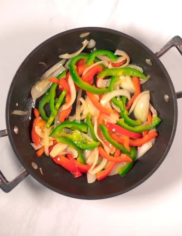 Onions and bell peppers are sauteed in a pan.