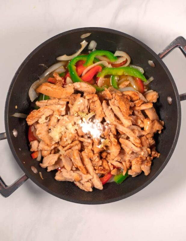 Marinated chicken and seasoning are added to the pan.