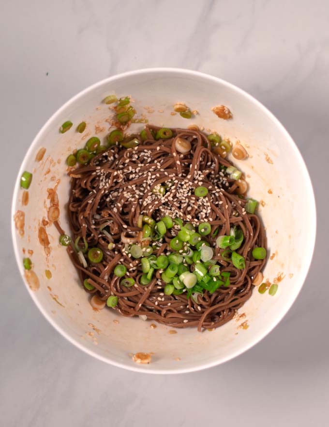 Soba Noodles mixed with sauce and garnished with scallions and sesame seeds.