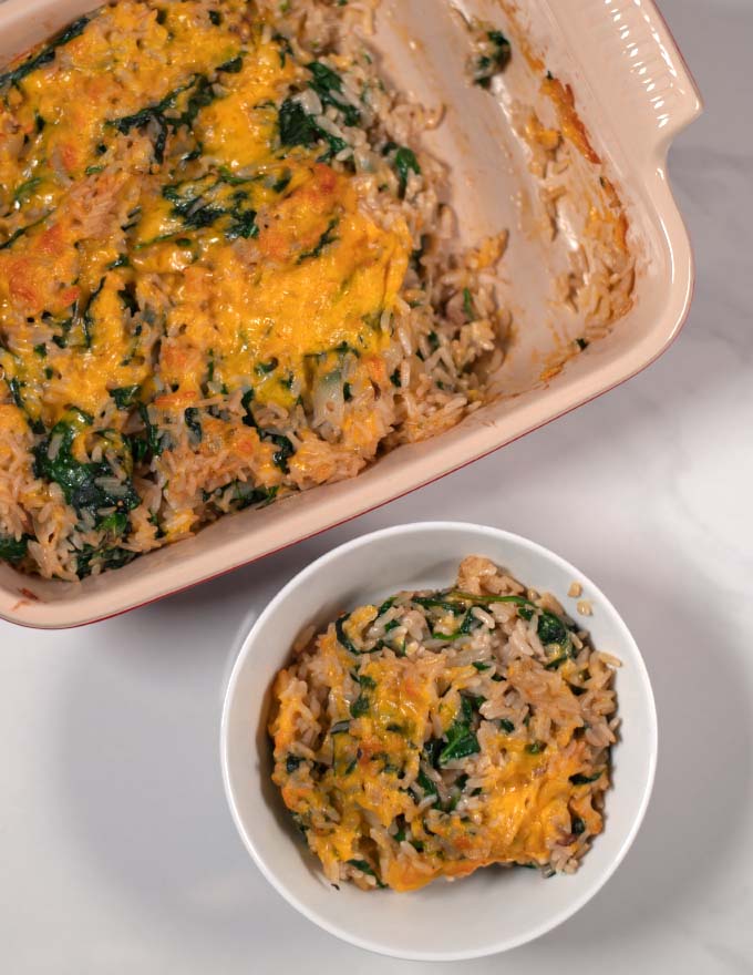 A serving of Spinach Rice Casserole in a bowl with the casserole dish in the background.