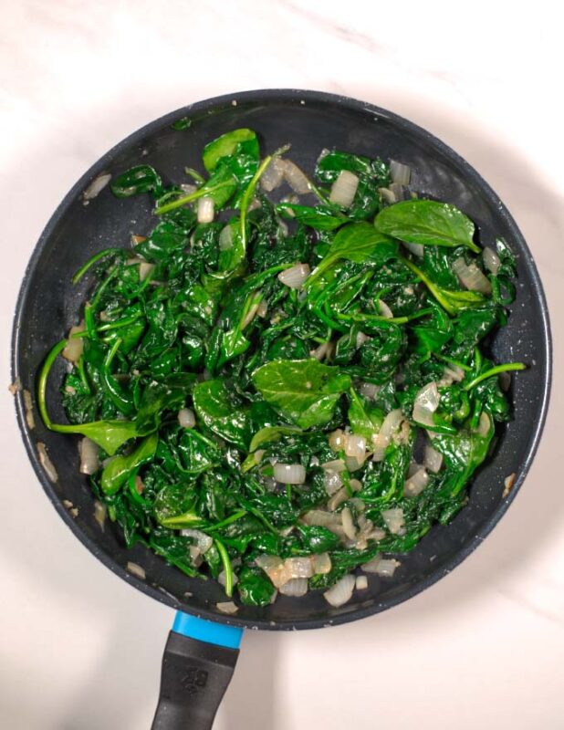 View of a pan with cooked onions and spinach.