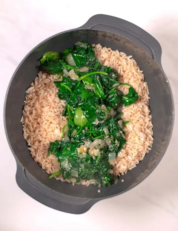 The sauteed spinach is given into a mixing bowl with precooked rice.