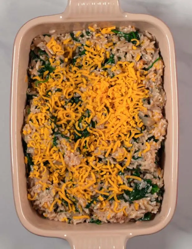 Spinach Rice Casserole mixture in a baking dish topped with vegan cheese.